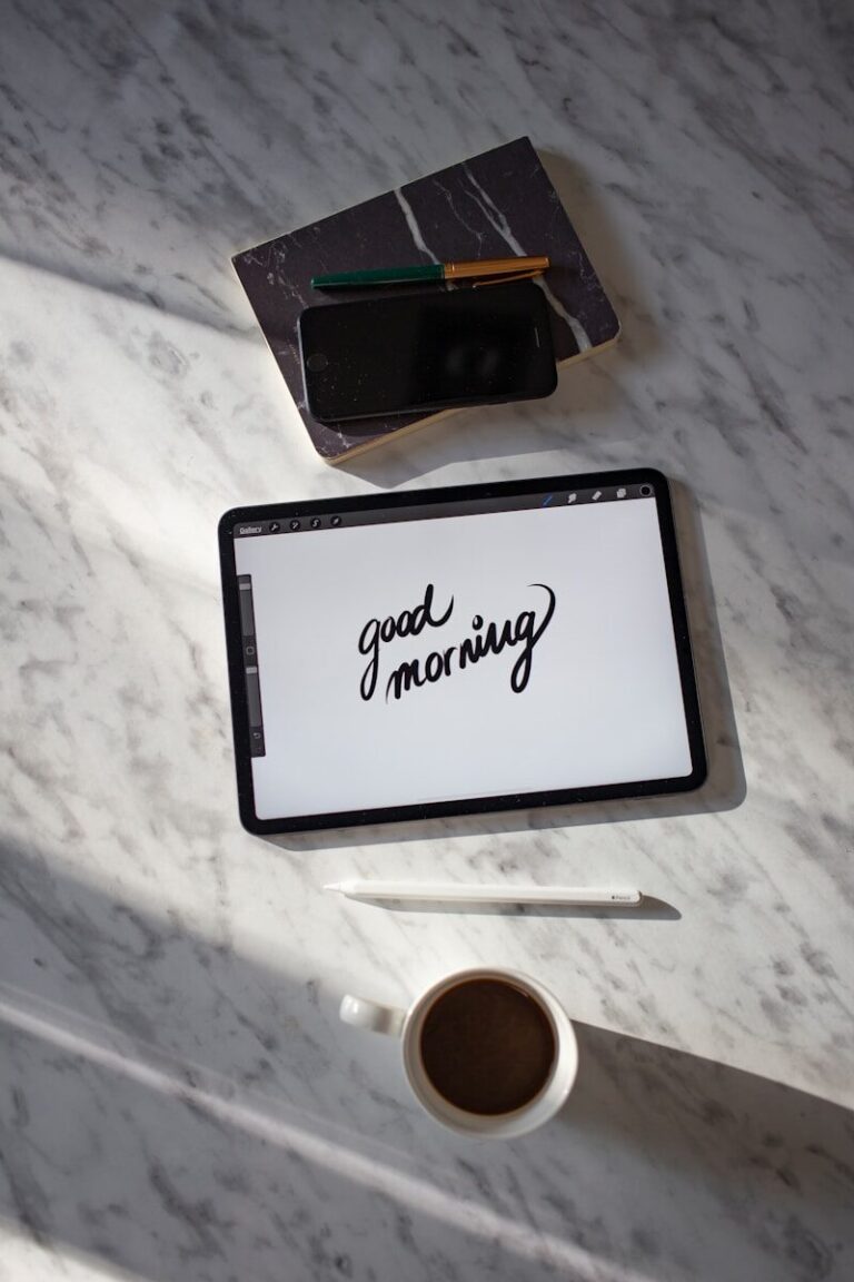 black tablet computer beside white ceramic mug on white table