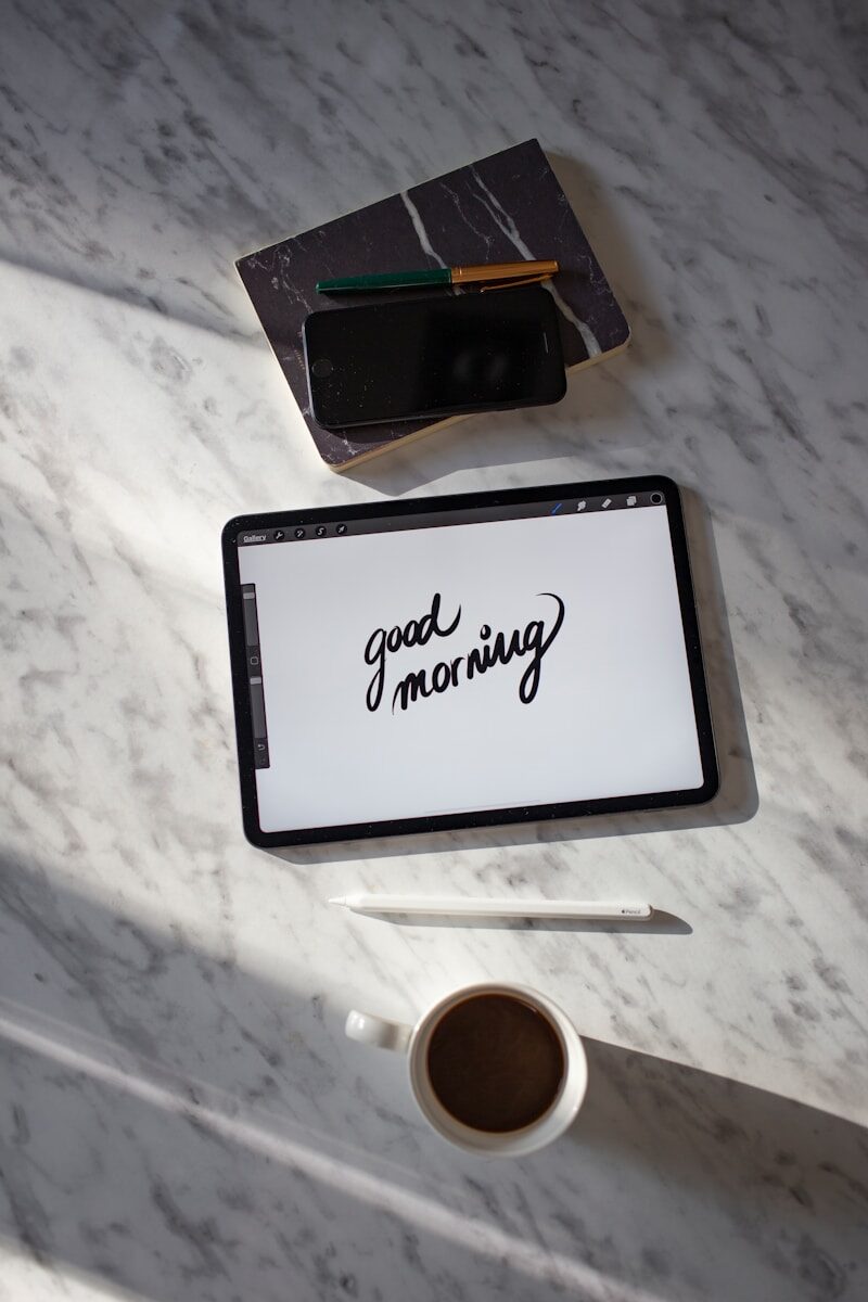 black tablet computer beside white ceramic mug on white table